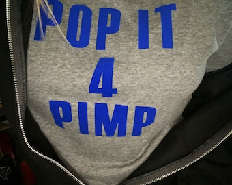 Op de afbeelding: Een grijs T-shirt met de tekst "POP IT 4 PIMP" in blauwe letters.