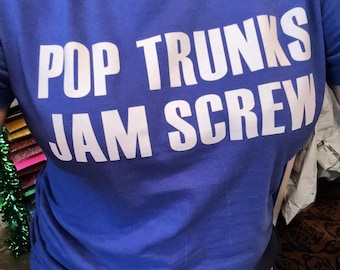 Op de afbeelding: Een koningsblauw t-shirt met de woorden "POP TRUNKS JAM SCREW" in grote witte hoofdletters gedrukt. Het shirt is gemaakt van een zacht materiaal en wordt gedragen.