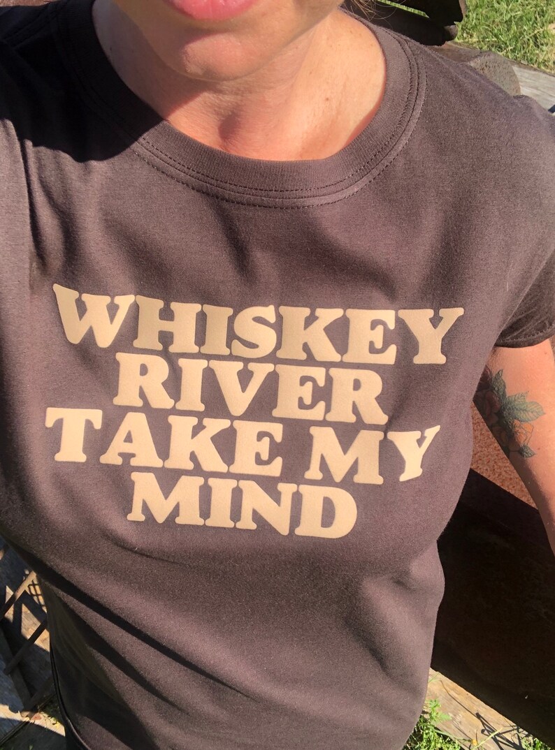 Peut inclure: Un t-shirt gris fonc&eacute; avec le texte "Whiskey River Take My Mind" imprim&eacute; en beige clair.