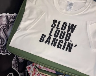 Op de afbeelding: Wit T-shirt met zwarte tekst die "Slow Loud & Bangin'" luidt, gedrukt op de voorkant.