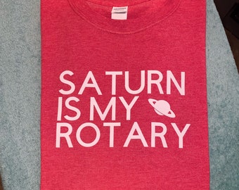 Op de afbeelding: Een rood t-shirt met witte tekst die "Saturn is my Rotary" luidt, met een klein wit beeld van Saturnus naast het woord "my".