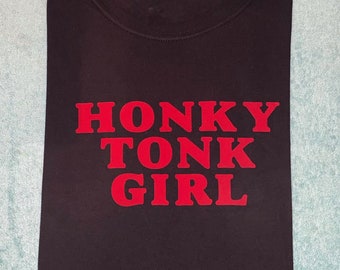 Op de afbeelding: Zwart T-shirt met de tekst "Honky Tonk Girl" in rood gedrukt.
