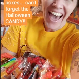 Puede incluir: Una mujer con una camiseta amarilla sostiene una gran bolsa de caramelos de Halloween surtidos. La bolsa est&aacute; llena de caramelos envueltos individualmente en varios colores, incluidos rojo, naranja, amarillo y verde. El texto en la imagen dice "??? BOXES! 46w Packing up Halloween mystery boxes... can't forget the Halloween CANDY!!"
