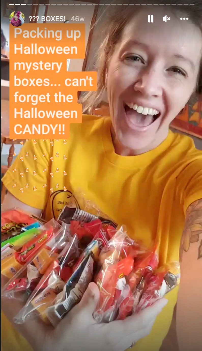 Puede incluir: Una mujer con una camiseta amarilla sostiene una gran bolsa de caramelos de Halloween surtidos. La bolsa est&aacute; llena de caramelos envueltos individualmente en varios colores, incluidos rojo, naranja, amarillo y verde. El texto en la imagen dice "??? BOXES! 46w Packing up Halloween mystery boxes... can't forget the Halloween CANDY!!"