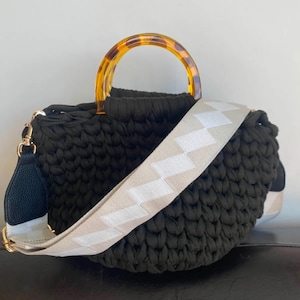 May include: Black crochet handbag with a tortoiseshell handle and a detachable cream and white patterned strap. The bag has a gold-tone clasp and a black leather accent on the strap.
