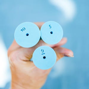 Może przedstawiać: Trzy niebieskie wałki z pianki z nadrukowanymi liczbami. Liczby to 10, 5 i 9/16.