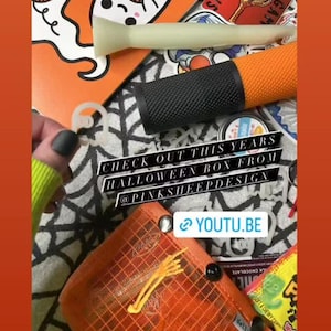 Puede incluir: Primer plano de una caja con tem&aacute;tica de Halloween con una variedad de art&iacute;culos, que incluyen una pegatina con forma de fantasma, un tee de golf, un cilindro negro y naranja y una peque&ntilde;a bolsa de malla naranja. El texto "CHECK OUT THIS YEARS HALLOWEEN BOX FROM @PINKSHEEPDESIGN" es visible en la caja. El texto "YOUTU.BE" tambi&eacute;n es visible.