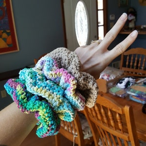 May include: A set of three crocheted hair scrunchies in a variety of colors, including teal, green, pink, and brown. The scrunchies are made with a soft, textured yarn and are perfect for adding a touch of style to any outfit.