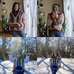 May include: A woman wearing a colorful crocheted hooded sweater with a striped pattern. The sweater has a large pocket on the front. The woman is standing in front of a window with white curtains.