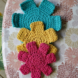 May include: Three crocheted flower-shaped pot holders in teal, yellow, and pink.