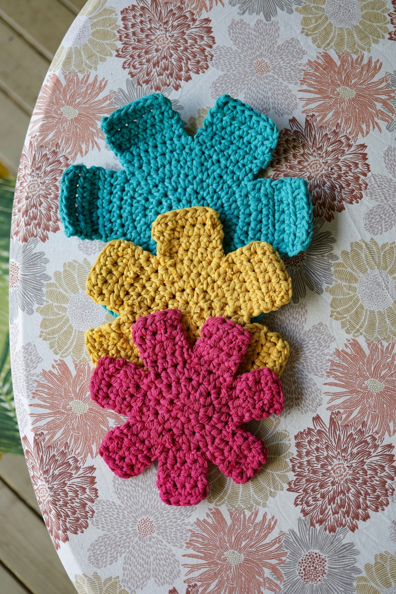 May include: Three crocheted flower-shaped pot holders in teal, yellow, and pink.