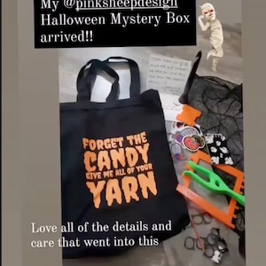Puede incluir: Una bolsa de tela negra con el texto "Forget the Candy Give me all of your Yarn" en naranja. La bolsa est&aacute; llena de varios art&iacute;culos de tem&aacute;tica de Halloween, incluyendo pegatinas, un peque&ntilde;o fantasma de ganchillo y un par de agujas de tejer.