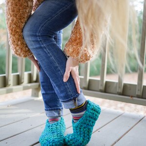 May include: A pair of teal blue crocheted slippers with a fuzzy brown sweater and blue jeans.