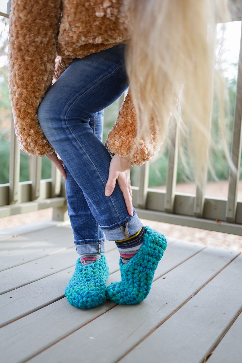 May include: A pair of teal blue crocheted slippers with a fuzzy brown sweater and blue jeans.