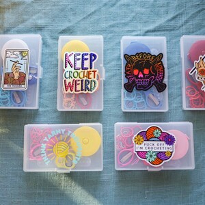 Pode incluir: Seis recipientes de pl&aacute;stico transparente com adesivos e suprimentos tem&aacute;ticos de croch&ecirc; coloridos. Os adesivos incluem "Keep Crochet Weird", "Death Before Knitting", "Think Yarn Think" e "Fuck Off I'm Crocheting".