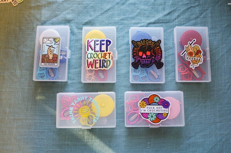 Pode incluir: Seis recipientes de pl&aacute;stico transparente com adesivos e suprimentos tem&aacute;ticos de croch&ecirc; coloridos. Os adesivos incluem "Keep Crochet Weird", "Death Before Knitting", "Think Yarn Think" e "Fuck Off I'm Crocheting".