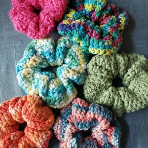May include: Six colorful crocheted hair scrunchies in various colors including pink, green, blue, orange, and gray.