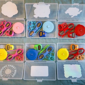 Pode incluir: Seis recipientes de pl&aacute;stico transparente com tampas, cada um contendo um conjunto de ferramentas de costura e tric&ocirc; coloridas. Os recipientes s&atilde;o etiquetados com as palavras "Think Yarn" e "Yarn Thought".