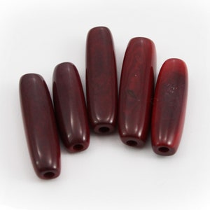 May include: Five dark red wooden beads, each with a smooth, oval shape and a hole drilled through the center.