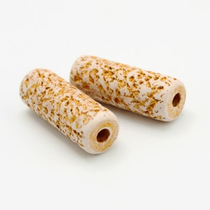 Peut inclure: Deux perles en céramique cylindriques beige et brunes avec une texture rugueuse.