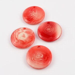 Könnte beinhalten: Vier runde, rot-cremefarbene Anhänger mit einem Wirbelmuster und einem kleinen Loch oben. Die Anhänger sind auf weißem Hintergrund angeordnet. Diese Anhänger eignen sich für die Schmuckherstellung.