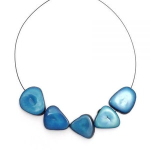 May include: A necklace featuring six polished, irregular-shaped blue beads strung on a thin, dark cord. The beads have a glossy finish and vary slightly in shade, creating a subtle visual texture. The necklace is displayed against a white background.