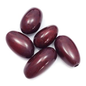 Peut inclure: Cinq perles ovales de couleur marron, avec une finition brillante, sont disposées sur un fond blanc. Chaque perle a un petit trou à une extrémité. Les perles sont lisses et réfléchissent la lumière.