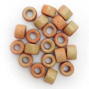 Op de afbeelding: Een groep terracotta en beige keramische kralen met een gat in het midden. De kralen zijn verspreid over een wit oppervlak.