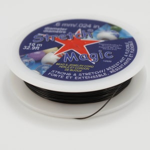 Puede incluir: Un carrete blanco de cordón negro Stretch Magic para abalorios y joyería. La etiqueta azul y roja tiene el texto "Stretch Magic" y "6 mm/.024 in diámetro". El cordón mide 10 m de largo.