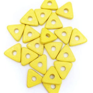 Puede incluir: Una colección de cuentas de madera de color amarillo en forma de triángulo con un agujero en el centro. Las cuentas están dispuestas en un patrón aleatorio.