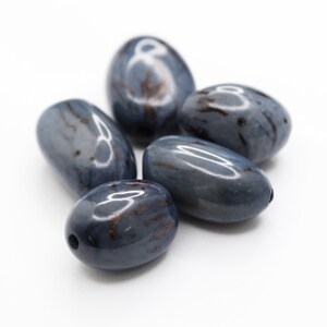 Peut inclure: Cinq pierres lisses de forme ovale avec un glacis bleu-gris et des marbrures brunes. Les pierres sont disposées en grappe sur un fond blanc.