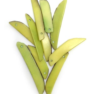 May include: A collection of elongated, tapered lime green shell pendants arranged in a cluster. Each piece features a smooth, matte finish with a single small circular hole drilled near the top edge for stringing, showcasing natural variations.