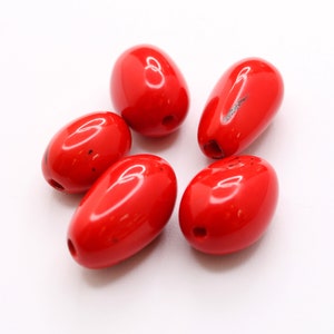 Peut inclure: Six perles ovales de couleur rouge avec un trou au centre. Les perles sont brillantes et lisses.