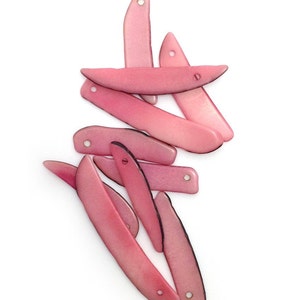 Può includere: Una collezione di perline rosa, curve e allungate, con un foro a un'estremità. Le perline hanno una finitura lucida e un bordo più scuro, sparse su uno sfondo bianco. Queste perline sono adatte per la creazione di gioielli.