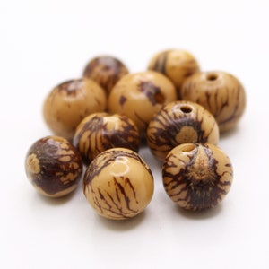May include: A group of natural brown and cream coloured beads with dark brown markings. The beads are round and have a hole through the centre.