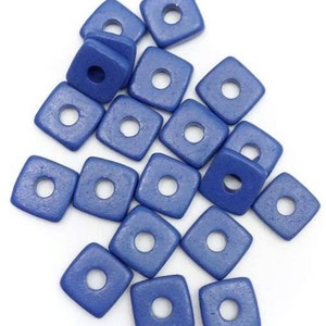 Può includere: Una collezione di perline quadrate blu con un foro centrale. Le perline sono sparse su uno sfondo bianco. Queste perline sono probabilmente utilizzate per la creazione di gioielli o altri progetti artigianali.