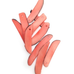 Può includere: Una collezione di perline curve color corallo con un bordo scuro e un foro a un'estremità. Le perline sono disposte su uno sfondo bianco. Queste perline sono adatte per la creazione di gioielli e l'artigianato.