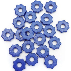 Può includere: Una collezione di piccole perline di legno blu scuro a forma di stella, con un foro centrale. Le perline sono sparse su una superficie bianca, mostrando la loro forma e colore unici. Ideale per l'artigianato e la creazione di gioielli.