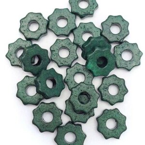 Può includere: Una collezione di perline a forma di stella, di colore verde scuro, con un foro centrale. Le perline hanno una superficie strutturata e sono sparse su uno sfondo bianco. Queste perline sono probabilmente per la creazione di gioielli o altri lavori artigianali.