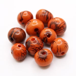 May include: A group of ten orange and brown seed beads with black markings. The beads have a hole in the centre for stringing.