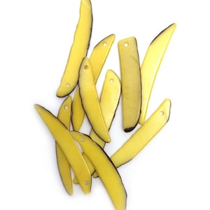 Könnte beinhalten: Eine Sammlung gelber, länglicher Perlen mit einem dunkelbraunen Rand und einem Loch an einem Ende. Die Perlen sind auf weißem Hintergrund verstreut. Die Perlen sind etwa 5 cm lang.