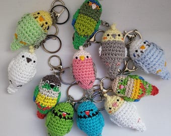 Può includere: Una collezione di 11 portachiavi a forma di parrocchetto all'uncinetto in vari colori, tra cui verde, blu, rosa, bianco e grigio. Ogni portachiavi presenta un piccolo parrocchetto all'uncinetto con un anello per chiavi attaccato.
