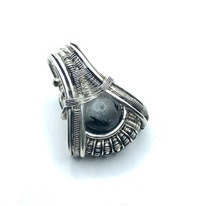 Può includere: Un ciondolo avvolto in filo d'argento con una pietra preziosa grigio scuro. Il ciondolo ha la forma di una lacrima e presenta un design delicato e intricato.