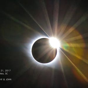May include: A photograph of a total solar eclipse with the sun's corona visible. The image was taken on August 21, 2017 in Columbia, SC. The text "DOROTHY & JOHN" is visible in the bottom left corner of the image.
