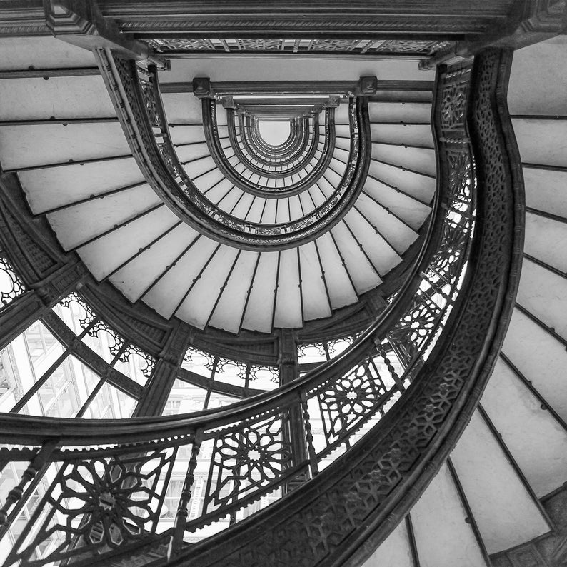 Puede incluir: Una fotograf&iacute;a en blanco y negro de una escalera de caracol con intrincadas barandillas de metal. La escalera est&aacute; hecha de m&aacute;rmol blanco y tiene una gran ventana en la parte superior.