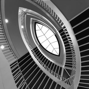 Puede incluir: Una fotograf&iacute;a en blanco y negro de una escalera de caracol con un gran tragaluz redondo en el centro. La escalera est&aacute; hecha de metal y tiene un dise&ntilde;o moderno.
