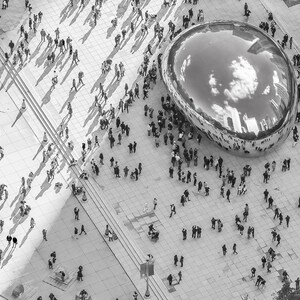 May include: A black and white aerial view of a large, reflective, silver sculpture in the shape of a bean. The sculpture is surrounded by a crowd of people.