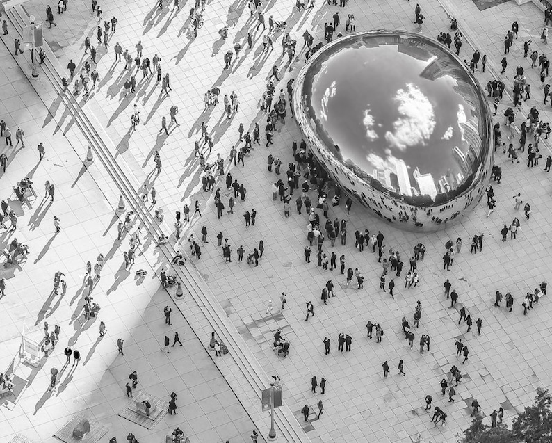May include: A black and white aerial view of a large, reflective, silver sculpture in the shape of a bean. The sculpture is surrounded by a crowd of people.