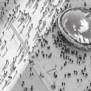 May include: An aerial view of a large, reflective, bean-shaped sculpture in a public square.  The sculpture is surrounded by people, and the sky is reflected in the sculpture's surface.