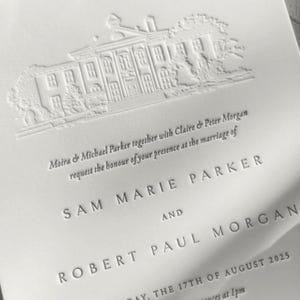 A close-up of the letterpress impression and texture on a wedding invitation with black ink letterpress text in a modern minimal and timeless serif font with a custom illustration of a wedding venue blind embossed/debossed showing texture on the thick white cotton card.